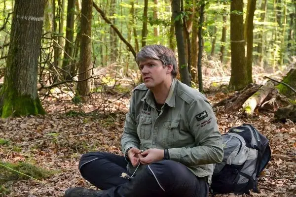 Mann sitzt im Wald auf dem Boden und hält eine Schnur in der Hand