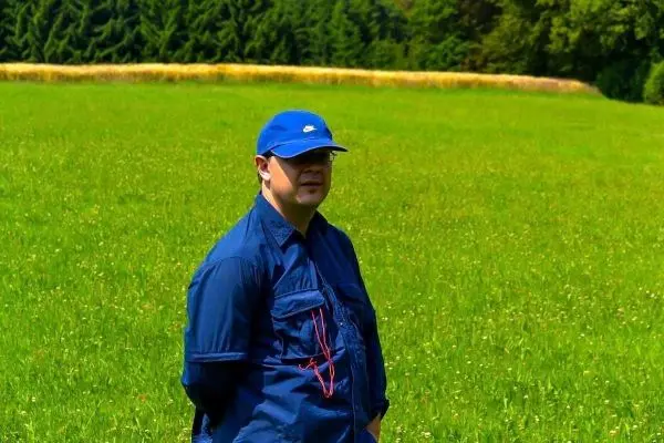 Mann steht in einem grünen Feld mit Bäumen im Hintergrund