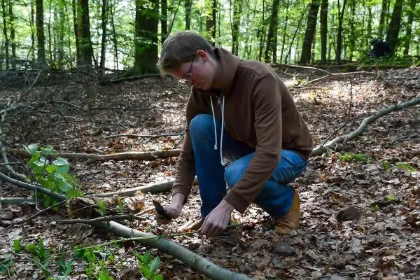 Messer bearbeitet Holzstück auf dem Waldboden zwischen Laub und Ästen