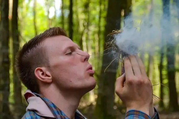 Person bläst auf ein Bündel trockener Gräser im Wald