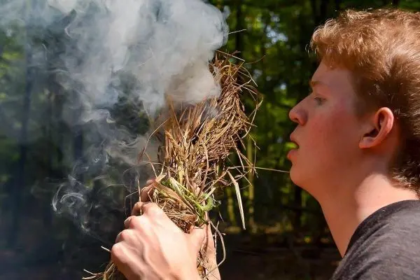 Person bläst in eine Ansammlung von trockenem Gras