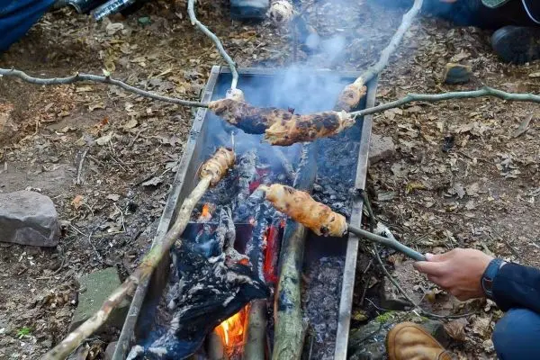 Person hält Stock über Feuer mit gebackenem Brotstück beim Überlebenstraining