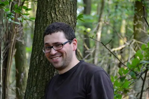 Person lehnt an Baumstamm im Wald und lächelt