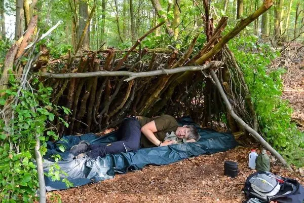 Person liegt in einer Tarp-Notunterkunft aus Ästen und Blättern