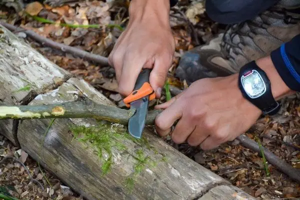 Person schneidet mit einem Messer einen Stock im Wald