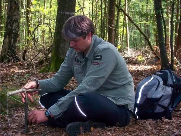 Person sitzt im Wald und baut eine Falle auf