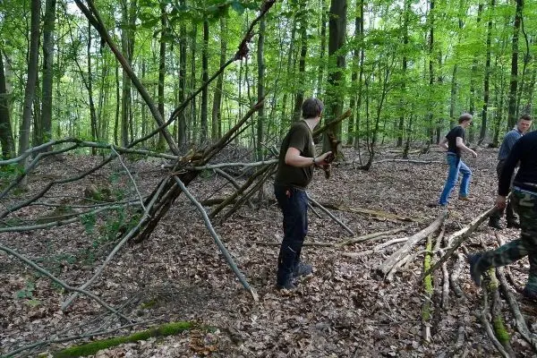 Person steht neben selbstgebauter Struktur im Wald