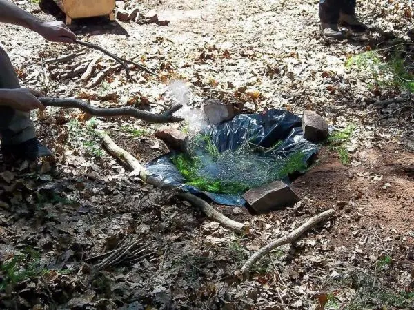 Rauch steigt aus improvisierter Wasserkochstelle mit Folie und Steinen auf
