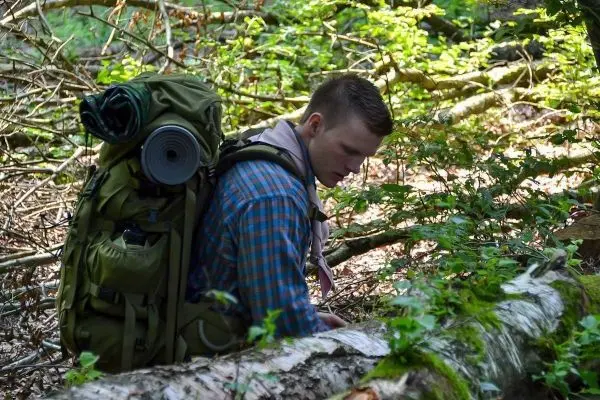 Rucksack mit Schlafmatte auf dem Rücken, untersucht umgestürzten Baumstamm