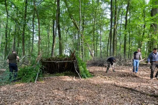 Selbstgebaute Tarp-Notunterkunft im Wald, Teilnehmer sammeln Äste und Laub