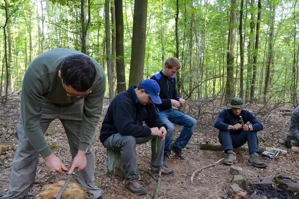 Teilnehmer bearbeiten Holzstücke mit Messern im Wald