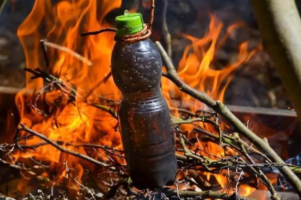 Wasserflasche hängt über einem kleinen Feuer aus Ästen