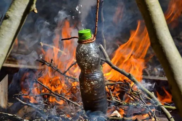 Wasserflasche über Feuer zum Abkochen aufgestellt, Rauch und Flammen sichtbar
