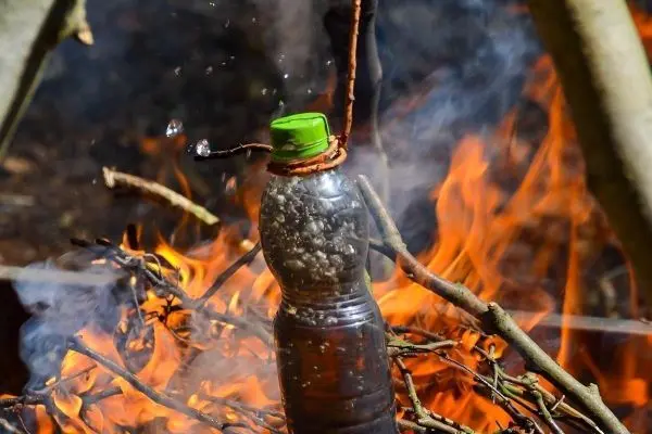 Wasserkochen in Plastikflasche über Feuer mit Zweigen und Dampf