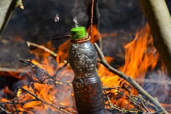 Wasserkochen in Plastikflasche über offenem Feuer mit sprudelndem Wasser