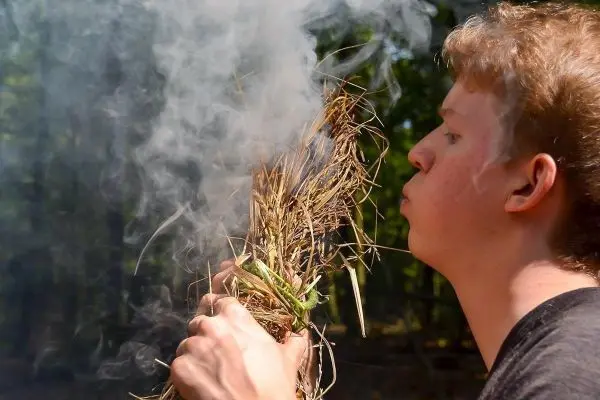 Zunder glimmt, Rauch steigt auf, Person bläst vorsichtig darauf
