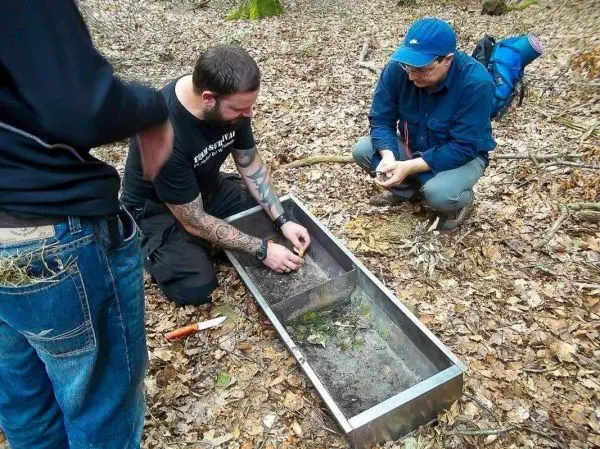 Zwei Personen arbeiten an einer improvisierten Feuerstelle aus Metall im Wald