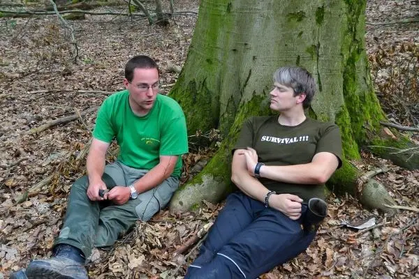 Zwei Personen sitzen am Stamm eines Baumes im Laub