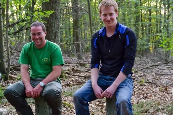 Zwei Personen sitzen auf Baumstümpfen im Wald