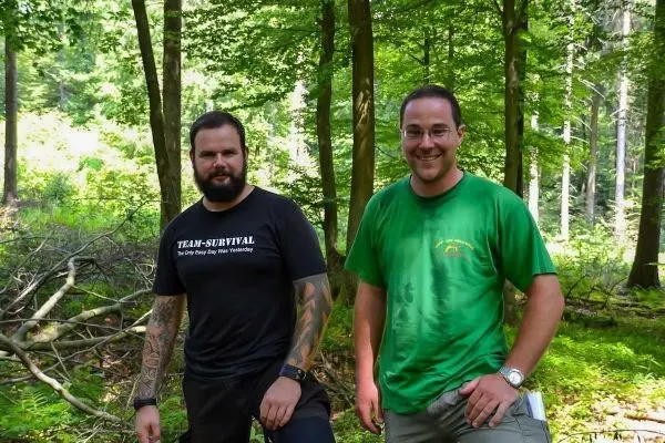 Zwei Personen stehen im Wald zwischen Bäumen und Ästen