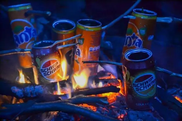 Dosen stehen auf einem Holzstapel über einem kleinen Bodenfeuer