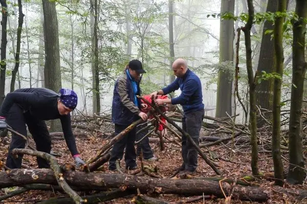 Drei Personen bauen eine Konstruktion aus Ästen im Wald