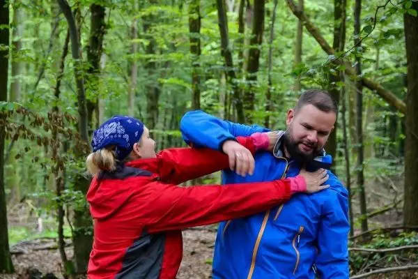 Eine Person in roter Jacke übt einen Griff an einer Person in blauer Jacke im Wald aus