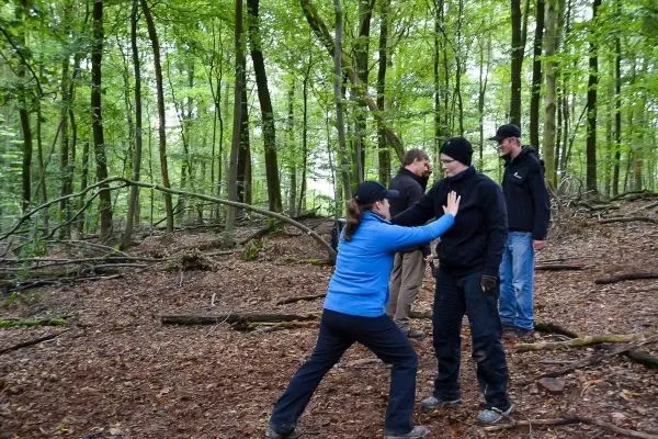 Eine Person übt eine Selbstverteidigungstechnik im Wald mit drei weiteren Personen