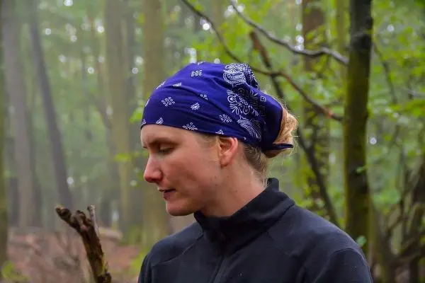 Frau mit blauer Bandana betrachtet einen Stock im Wald