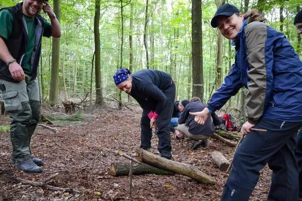 Gruppe arbeitet im Wald an einer Holzstruktur mit mehreren Stämmen