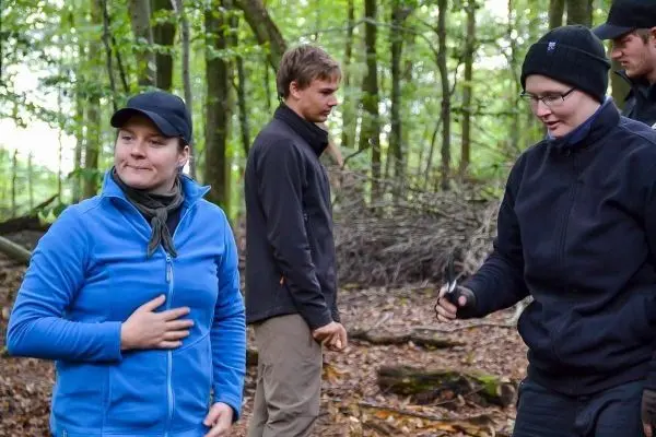 Gruppe im Wald steht um einen Haufen aus Ästen und Holz