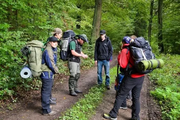 Gruppe mit Rucksäcken steht auf Waldweg und diskutiert Ausrüstung
