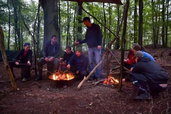 Gruppe sitzt um ein Feuer, einige halten Stöcke über die Flammen