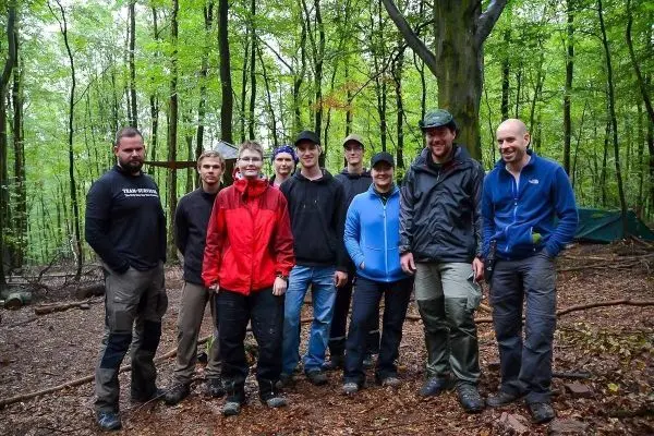 Gruppe von Personen in Outdoor-Bekleidung steht im Wald auf Laubboden