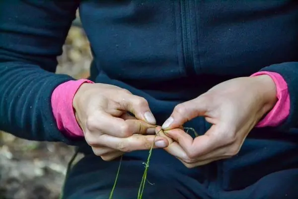 Hände flechten Pflanzenmaterial zu einer Schnur
