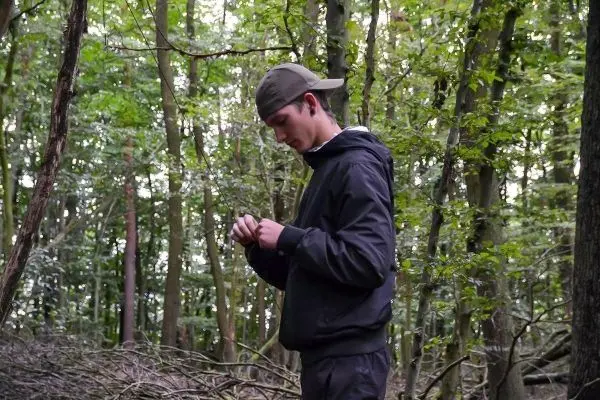 Junger Mann prüft Ausrüstung im Wald zwischen Bäumen und Ästen