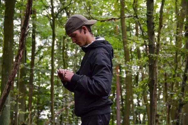 Junger Mann steht im Wald und betrachtet einen Gegenstand in seinen Händen