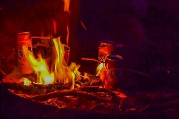 Kleine Flamme brennt zwischen Holzstücken und Dosen