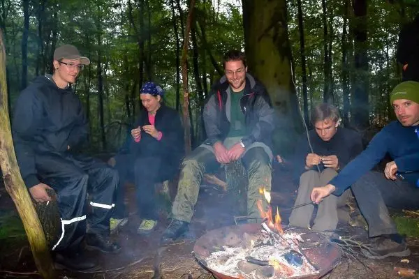 Kleines Bodenfeuer in einer Feuerschale umringt von mehreren Personen im Wald