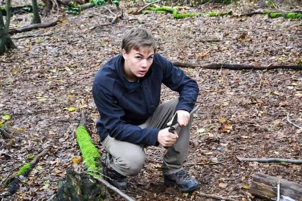 Kniend bearbeitet ein Messer einen Holzstock im Wald