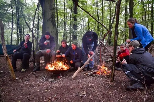 Lagerfeuer brennt in einer improvisierten Feuerstelle, Teilnehmer bereiten Essen zu
