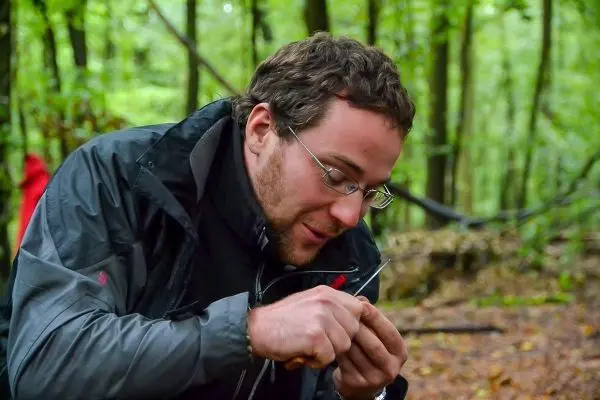 Mann bearbeitet ein kleines Holzstück mit einem Messer im Wald
