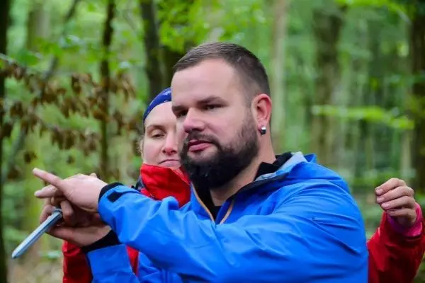 Mann zeigt mit einem Messer auf einen Punkt im Wald
