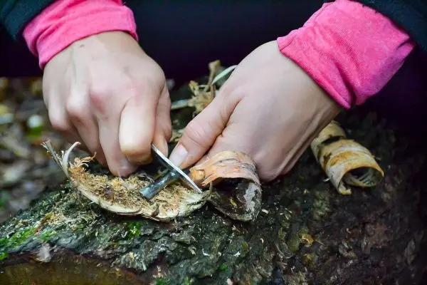 Messer schneidet Rinde von einem Holzstück zur Herstellung von Zunder