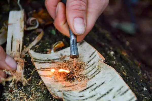 Person erzeugt Funken auf Rinde beim Feuerentfachen im Outdoorkurs
