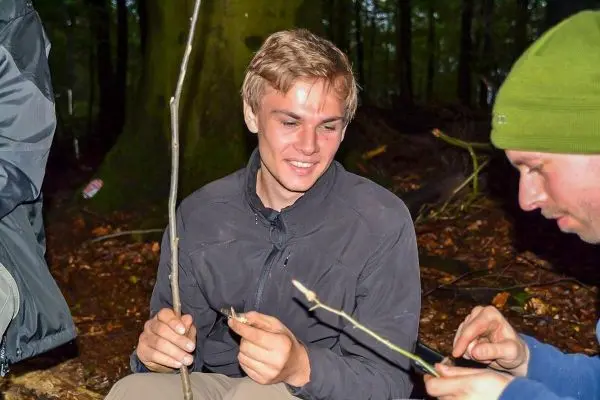 Person hält einen Stock und schaut lächelnd zu einer anderen Person