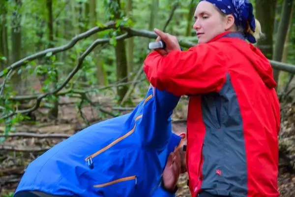 Person hilft anderer Person beim Abseilen im Wald
