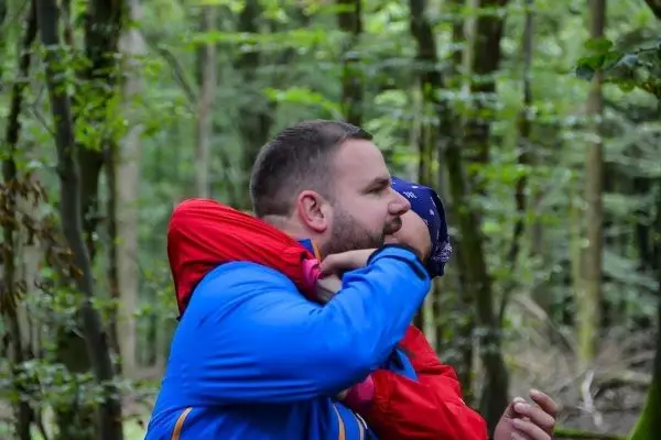 Person trägt Kind auf dem Rücken im Wald