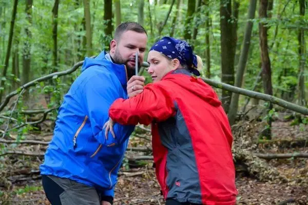 Person zeigt einer anderen Person eine Technik im Wald