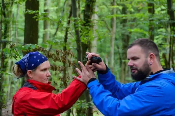 Person zeigt einer anderen Person eine Technik im Wald